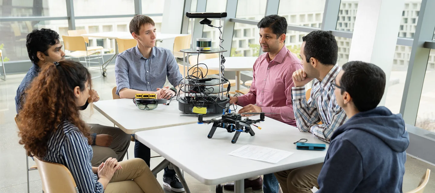 Researchers discussing aerial robots around a table in the lab